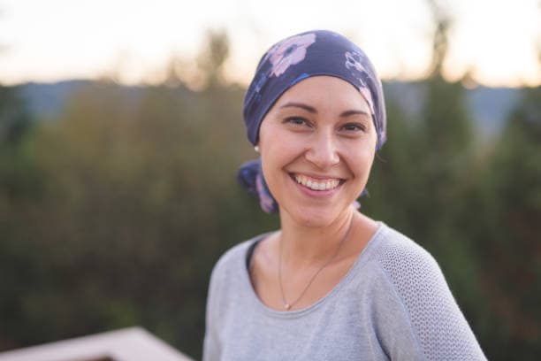Femme souriante en extérieur, portant un foulard, illustrant les soins de support